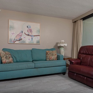This cozy living area features a teal sofa, a recliner, and a stunning beachfront view through large windows