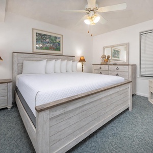 Bright and airy bedroom featuring a king bed, stylish wooden furniture, a TV, and a cozy lamp beside the nightstand