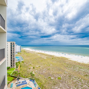 Balcony view showcasing the beach with white sand, turquoise gulf waters, and a glimpse of the pool area below
