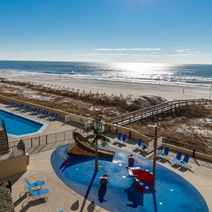 A vibrant pool area features a playful water park, surrounded by lounge chairs and offering a direct view of the beach