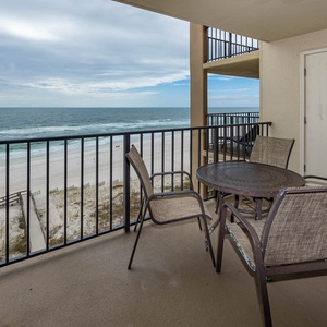 Relax on the balcony with a table and chairs, offering a beautiful view of the sandy beach and gentle waves