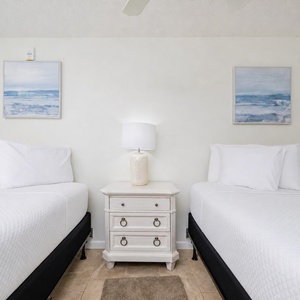 Two queen beds with crisp white linens and coastal artwork create a serene atmosphere in this inviting guest bedroom