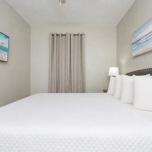 Brightly lit guest bedroom features a plush king bed with decorative pillows and a wall-mounted TV