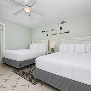 This guest bedroom features two queen beds, a ceiling fan, and nautical decor, creating a relaxed coastal atmosphere