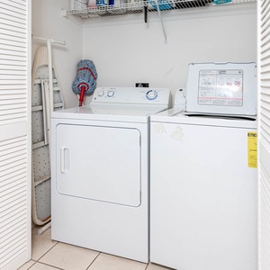 Laundry area featuring a washer and dryer, with an ironing board and cleaning supplies neatly organized on shelves above