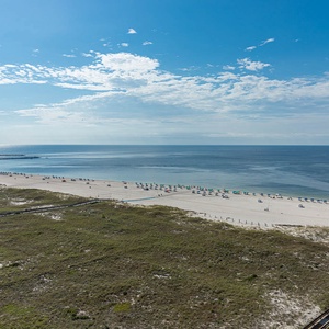 Expansive view of the beach with white sand, colorful umbrellas, and gentle waves under a clear blue sky