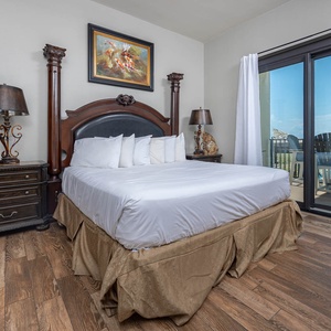 Elegant master suite featuring a king bed, stylish nightstands, and access to the balcony with views of the beach