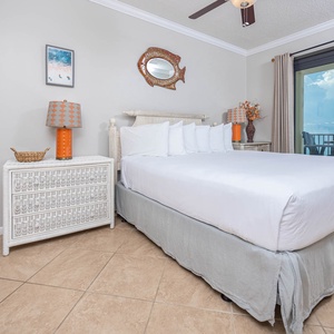 Cozy master bedroom features a king bed with white linens, colorful lamps, and direct access to a balcony with gulf views