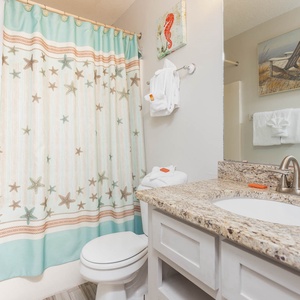 Guest bathroom features a starfish shower curtain, a granite countertop, and neatly arranged towels for a refreshing stay