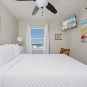 Queen bed in the guest suite invites restful sleep with coastal art and a calming view of the shore beyond the window