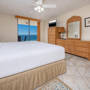 Cozy master bedroom featuring a plush king bed and a balcony with a view of the beach and inviting blue sky