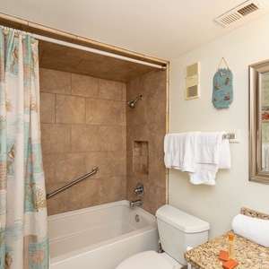 This bathroom features a tub-shower combo, a decorative curtain, granite countertop, and fresh towels for a refreshing stay