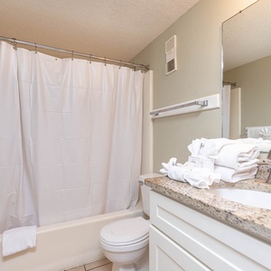 This bathroom features a clean design with a granite countertop, fresh towels, and a relaxing shower area