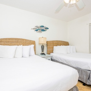 Sleep peacefully in this guest bedroom featuring two comfortable queen beds, beach-themed decor, and a ceiling fan