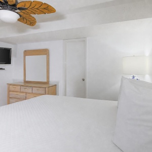 The bedroom features a plush king bed, a wall-mounted TV, a lighted dresser, and beach decor for a relaxed atmosphere