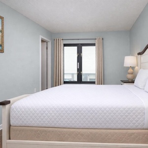 This guest bedroom features a queen bed, soft lighting, and a view through large windows, perfect for relaxation