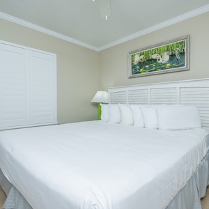 Relax in this serene guest bedroom featuring a king bed, soft linens, and cheerful artwork for a restful night's sleep