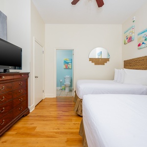 Guest room featuring two double beds, a flat-screen TV, and beach-themed artwork, creating a cheerful retreat
