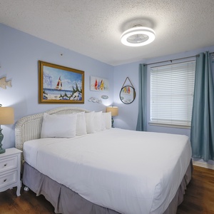 The master bedroom features a comfortable bed, beach-themed decor, and a bright, cheerful atmosphere