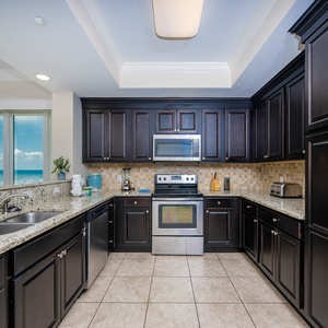 Prepare meals in the stylish kitchen featuring dark cabinetry, granite countertops, and expansive views of the beach