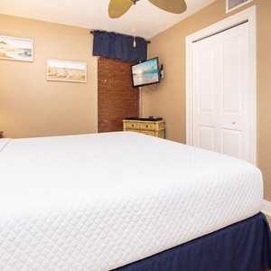 Cozy bedroom featuring a plush king bed, bedside lamp, wall-mounted TV, and warm-toned decor for a relaxing retreat