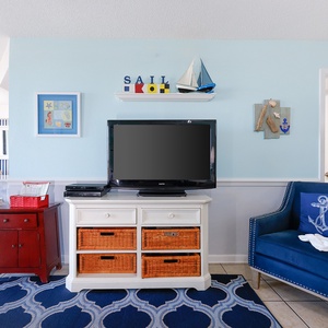 Brightly colored living area featuring a blue accent chair, a TV on a white cabinet, and nautical-themed decor