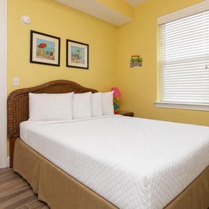 This cozy bedroom features a comfortable bed with white linens, cheerful yellow walls, and charming beach-themed decor