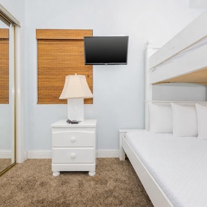 The guest bedroom features a white bunk bed, a bedside lamp, and a wall-mounted TV, perfect for relaxing after a day of fun