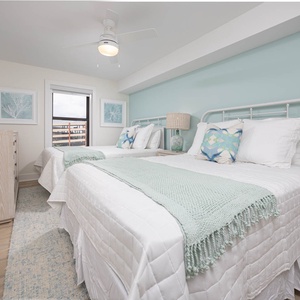 Guest bedroom featuring two queen beds with soft white linens, decorative pillows, and a view through the window
