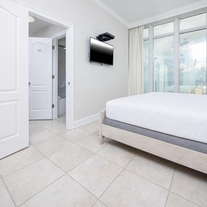 Relax in this inviting guest bedroom featuring a comfortable king bed, a mounted TV, and stunning beach views