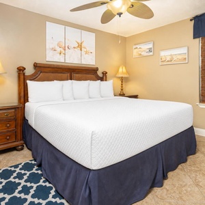 A cozy bedroom features a king bed with white linens, decorative artwork, and warm lighting from bedside lamps