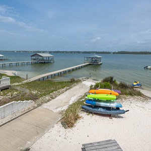 The serene view showcases colorful kayaks on the sandy shore, with tranquil lagoon waters and nearby docks inviting adventure