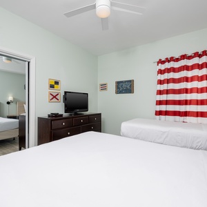 This guest bedroom features two beds, a queen and twin, a TV, and bright red striped curtains