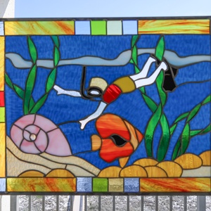 Colorful stained glass artwork depicting a snorkeler among marine life, with a view of the beach visible in the background
