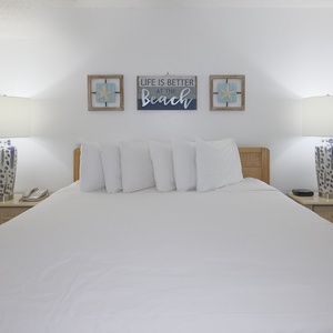 A king bed with white linens is flanked by blue and white lamps, complemented by beach wall art