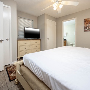 A cozy guest bedroom features a king bed, a dresser with a TV, and an adjoining bathroom visible through an open door