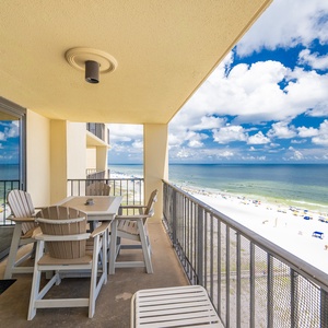 Balcony with patio dining table with chairs, offering a view of the vibrant beach and clear blue skies
