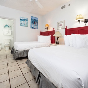 Guest bedroom featuring two double beds with red headboards, a bedside lamp, and beach artwork on the walls