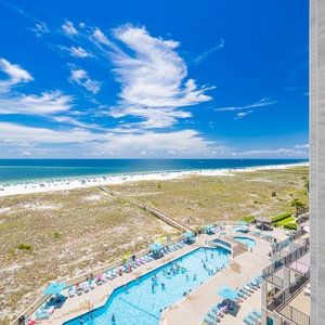 Balcony view showcases the inviting pool area alongside the beach, with vibrant umbrellas dotting the white sand shoreline