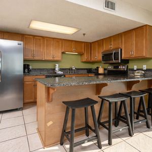 The kitchen features warm wooden cabinetry, a granite countertop, sleek stainless appliances, and bar seating