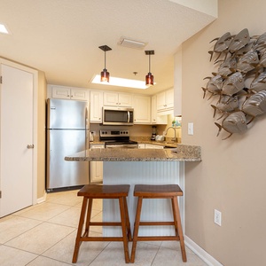 Kitchen area features a granite breakfast bar with two wooden stools and decorative wall art, creating a welcoming vibe