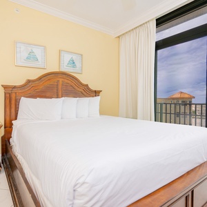 Guest bedroom featuring a cozy bed and large balcony doors showcasing a vibrant coastal view