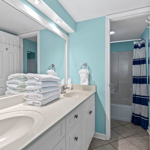 Master bathroom with a double vanity, fresh towels, and a shower/tub combo, accented by cheerful blue walls