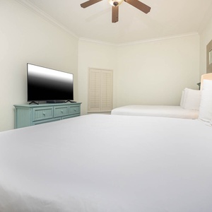 This guest bedroom features two queen beds, a TV for entertainment, and soft, neutral tones for a relaxing atmosphere