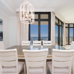 Bright dining area with elegant white chairs and panoramic views of the tranquil coastline through expansive windows