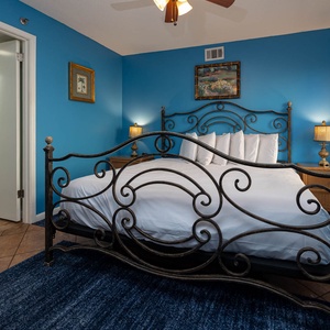 The guest bedroom features a wrought iron king bed with white linens, blue walls, and warm lighting from a bedside lamp