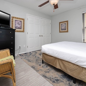 This cozy guest bedroom features a comfortable queen bed, a TV for entertainment, and charming decor with natural light