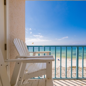 Two chairs on the balcony face a crystal-clear blue horizon where boats drift and colorful parasails float above the coast