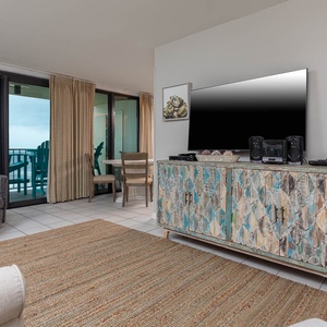 This inviting living area features a large TV, queen sofa-sleeper, colorful decor, and a view of the beachfront balcony