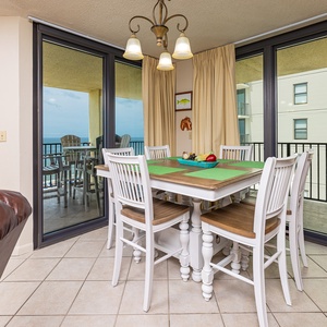 Bright dining area features a glass table with decorative fruit centerpiece, overlooking the beach through large windows